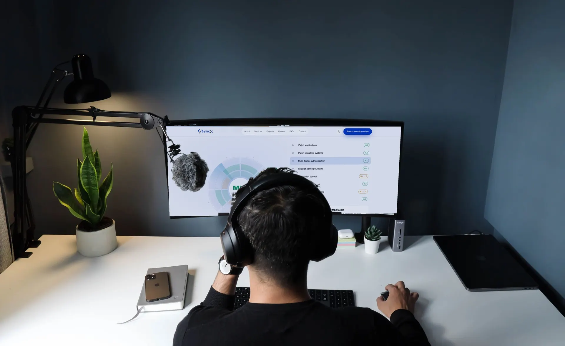 Engineer wearing headphones reviewing the SyncX Essential Eight view on a curved monitor
